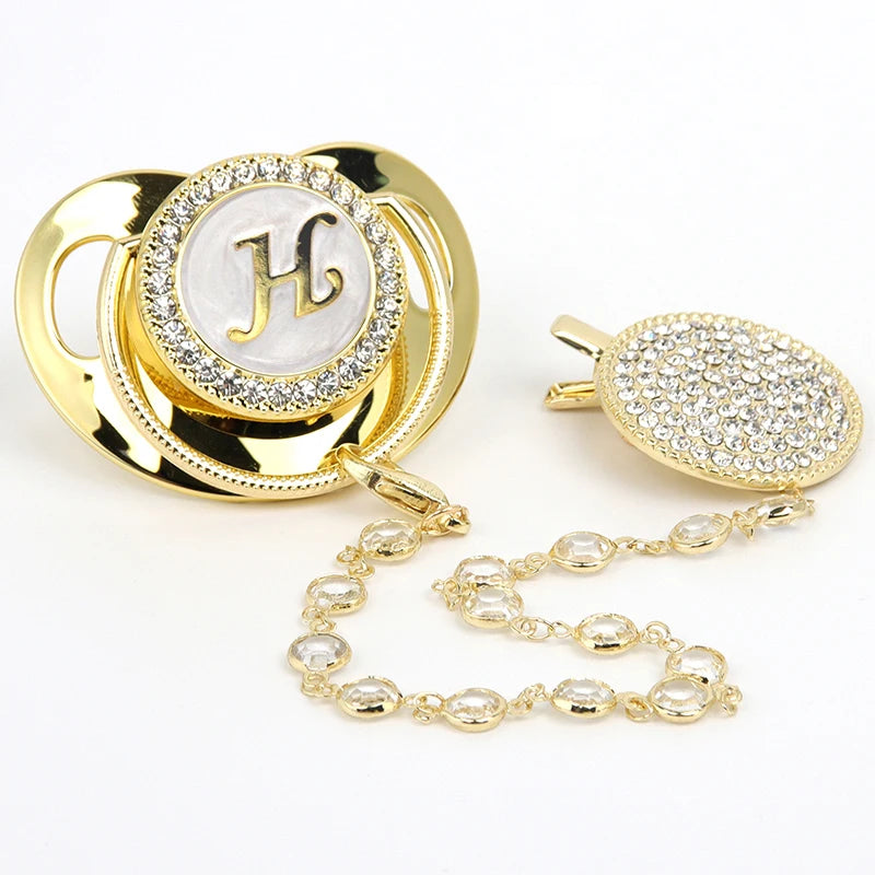 Gold and clear rhinestone pacifier featuring an initial H on a circular disc with a clip.