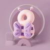A pink soft baby head protector pillow with purple adjustable straps is displayed on a light purple surface.