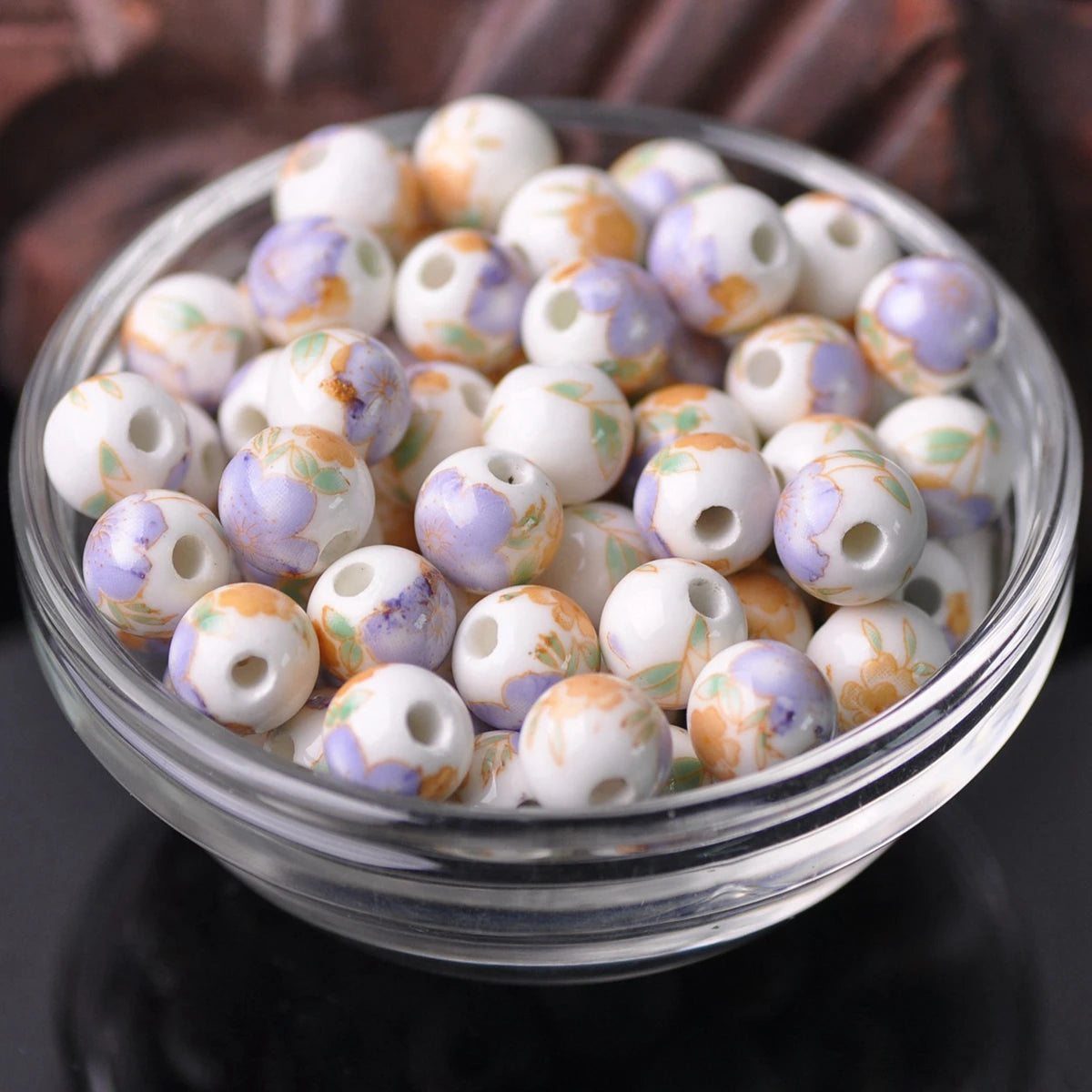 A bowl filled with small ceramic beads in shades of white and purple floral patterns for jewelry making