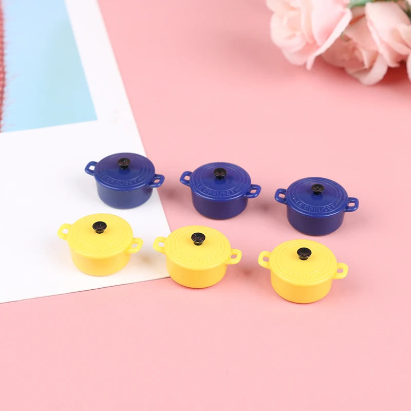 Five miniature copper soup pots in blue and yellow colors arranged on a pink background.