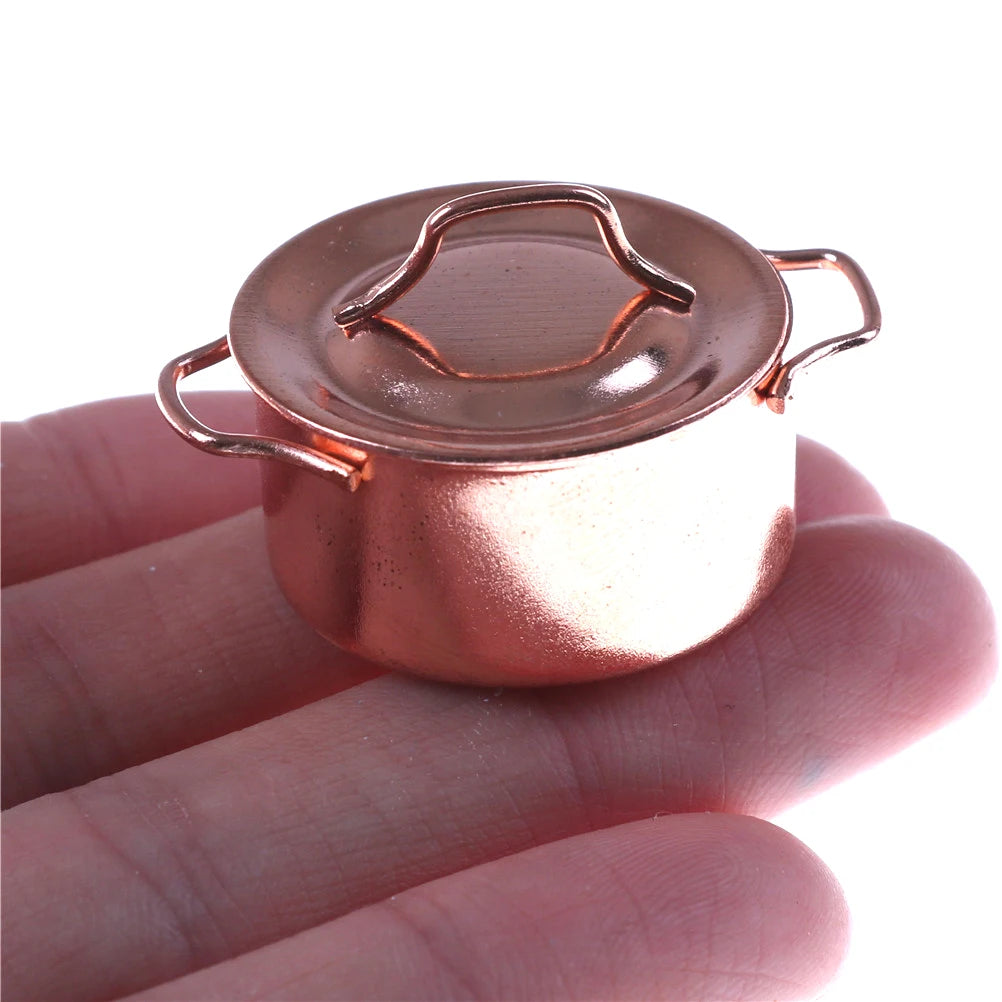 A miniature copper soup pot with a lid and handles is held in a person's hand.