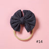 A dark gray knitted bow headband with a light yellow elastic band, photographed on a pink background.