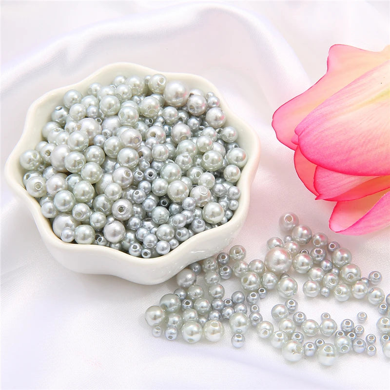 A white bowl filled with assorted silver and gray pearl beads, next to a pink lotus flower.