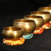 A collection of hammered copper singing bowls and mallets resting on a dark surface.