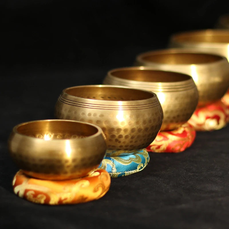 A collection of hammered copper singing bowls and mallets resting on a dark surface.