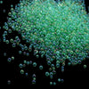 A pile of small, translucent green glass bubble beads scattered against a black background.