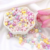 A pile of assorted pink, yellow, and iridescent pearl beads is displayed in a white dish with loose strands scattered nearby.