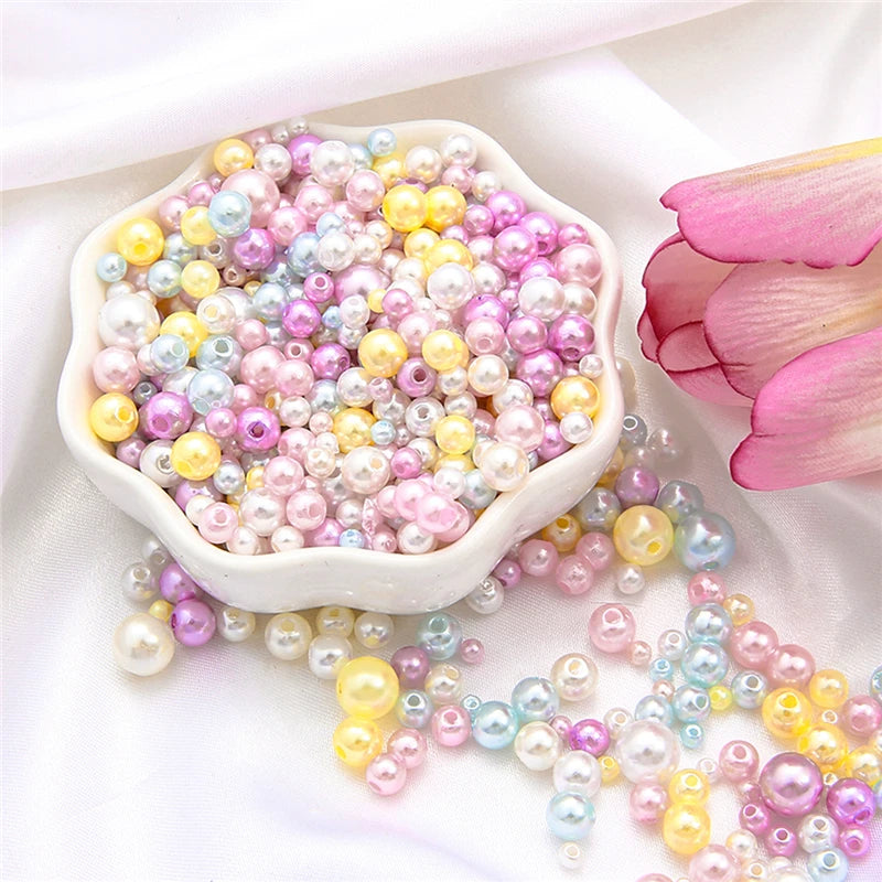 A pile of assorted pink, yellow, and iridescent pearl beads is displayed in a white dish with loose strands scattered nearby.