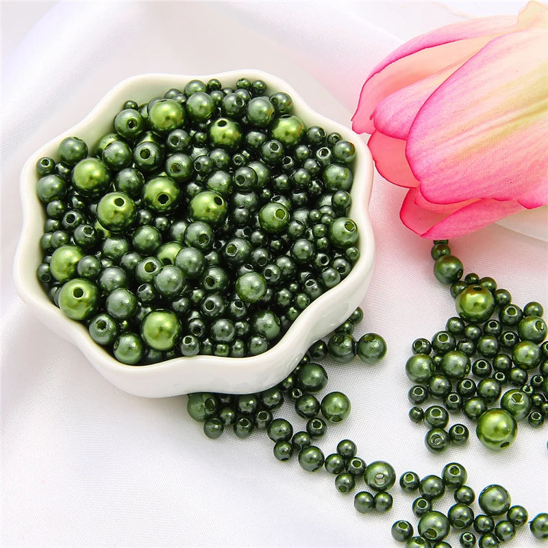 A white bowl filled with assorted green pearl beads next to a pink lotus flower.