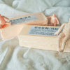 A light pink block of professional soft polymer clay used for sculpting and doll making, shown next to small human figures.