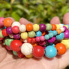 A collection of natural gemstone beads in various colors including orange, pink, green, yellow, and blue are held in a hand.