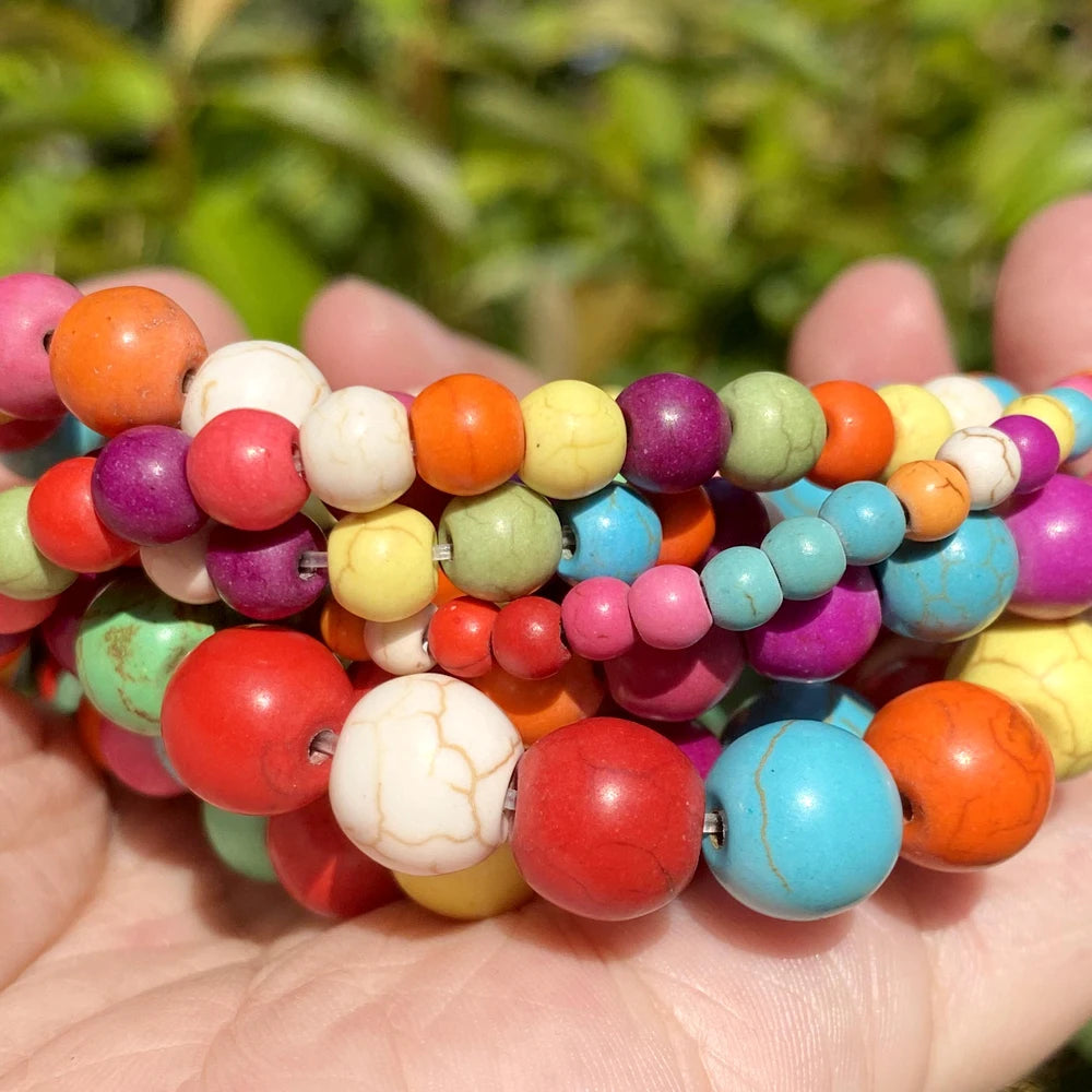 A collection of natural gemstone beads in various colors including orange, pink, green, yellow, and blue are held in a hand.