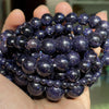 A hand holds a cluster of dark blue and purple natural gemstone beads for jewelry making.