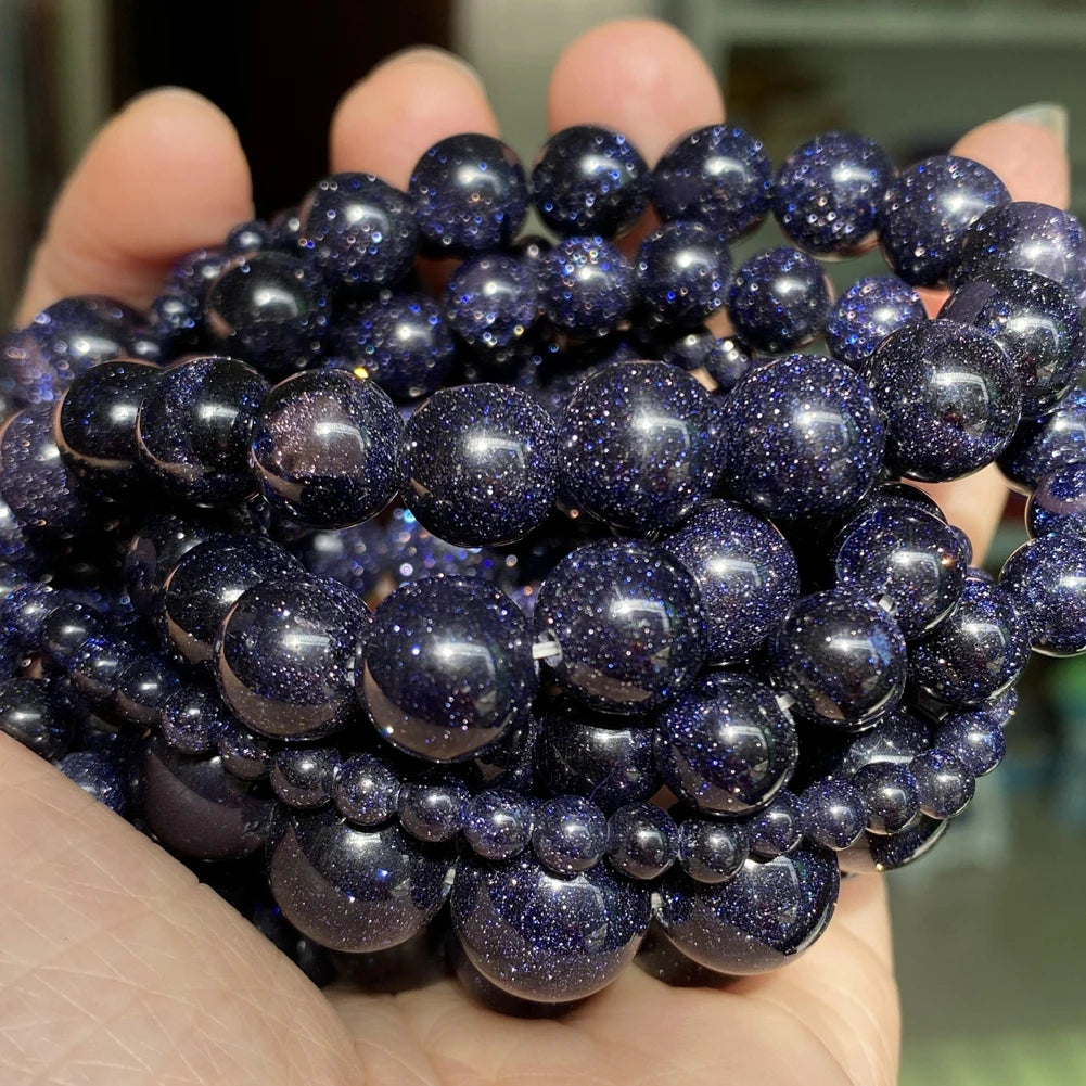 A hand holds a cluster of dark blue and purple natural gemstone beads for jewelry making.