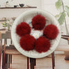 A white bowl filled with bright red, fluffy mink fur pom poms for crafts and accessories.