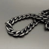 A close-up of a black acrylic bag chain strap with clips lying on a gray surface.