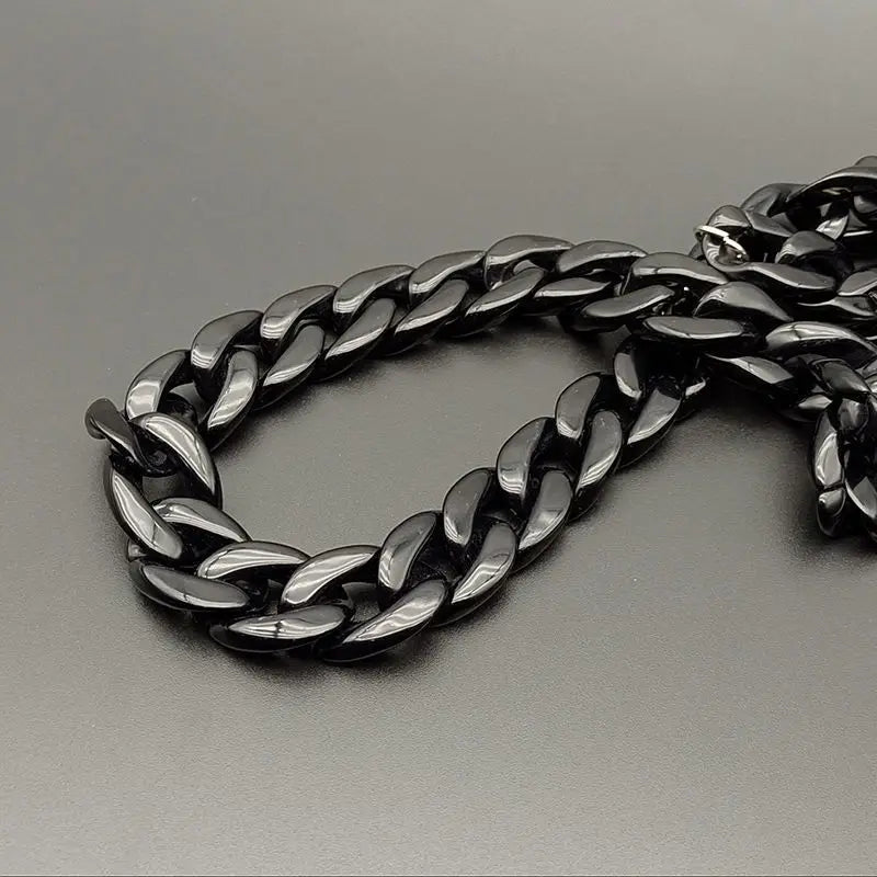 A close-up of a black acrylic bag chain strap with clips lying on a gray surface.