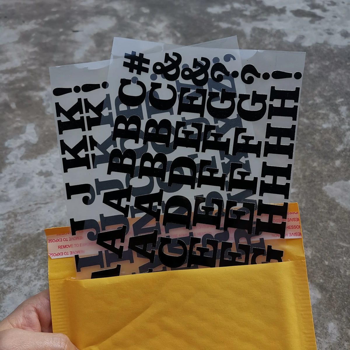 A hand holds a yellow envelope filled with black iron-on heat transfer patches for clothing.