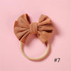 A soft, knitted orange-brown bow headband with a light yellow elastic band on a pink background.