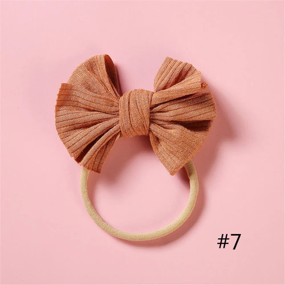 A soft, knitted orange-brown bow headband with a light yellow elastic band on a pink background.
