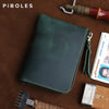 A dark green leather coin purse with a zipper is shown resting on brown leather and tools.