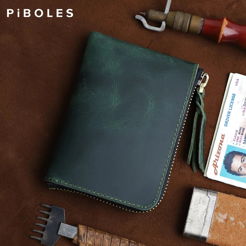 A dark green leather coin purse with a zipper is shown resting on brown leather and tools.