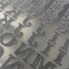Close-up of silver glitter iron-on heat transfer patches with various letters and symbols on a gray surface.