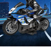 A blue and black 1:10 scale remote control stunt motorcycle is shown in a dynamic, low-angle shot against a dark background.