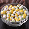 A bowl filled with small, round ceramic beads in yellow and green floral patterns for jewelry making