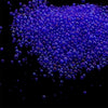 A pile of small, iridescent blue glass bubble beads scattered against a black background.