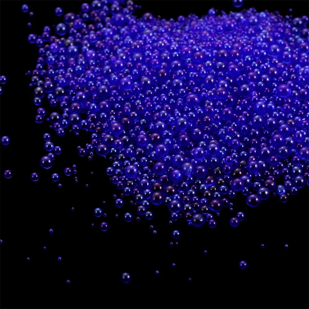 A pile of small, iridescent blue glass bubble beads scattered against a black background.