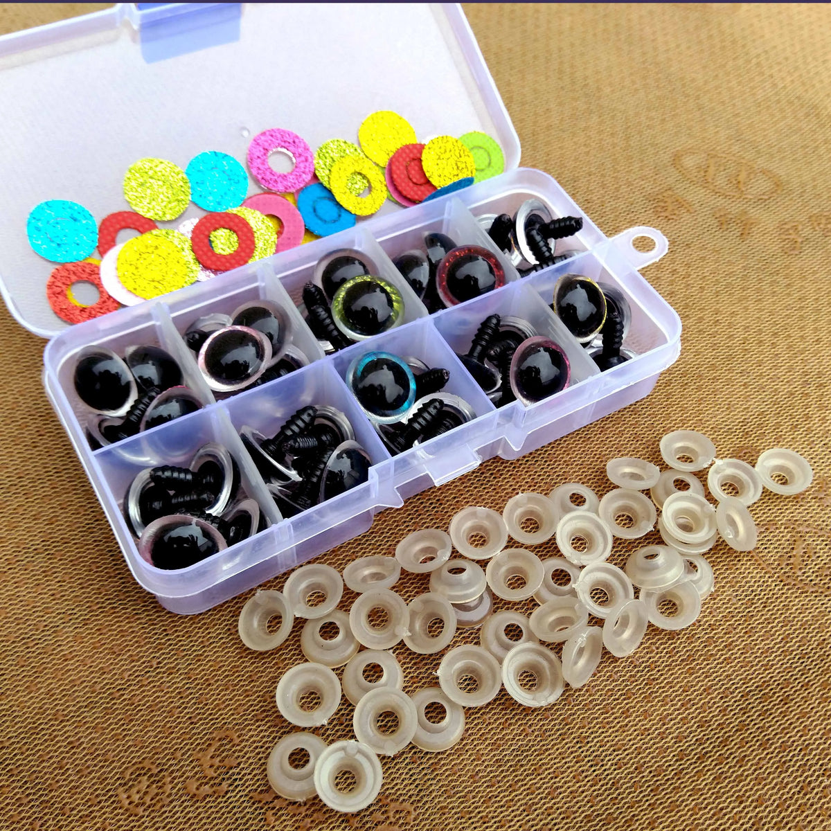 A clear plastic box filled with colorful plastic safety eyes for dolls and amigurumi, alongside loose white plastic eye parts