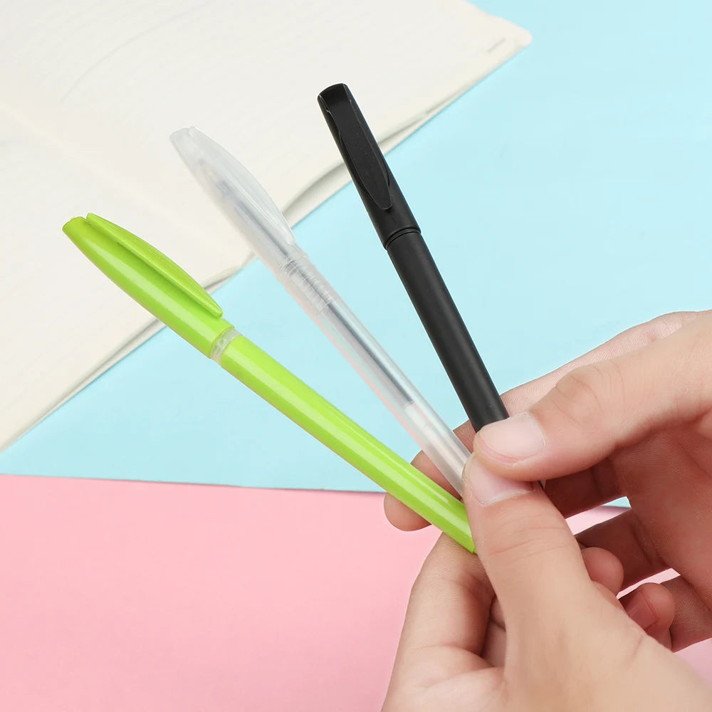 A hand holds three automatic fade pens, one green and two black, resting on pink and blue paper.