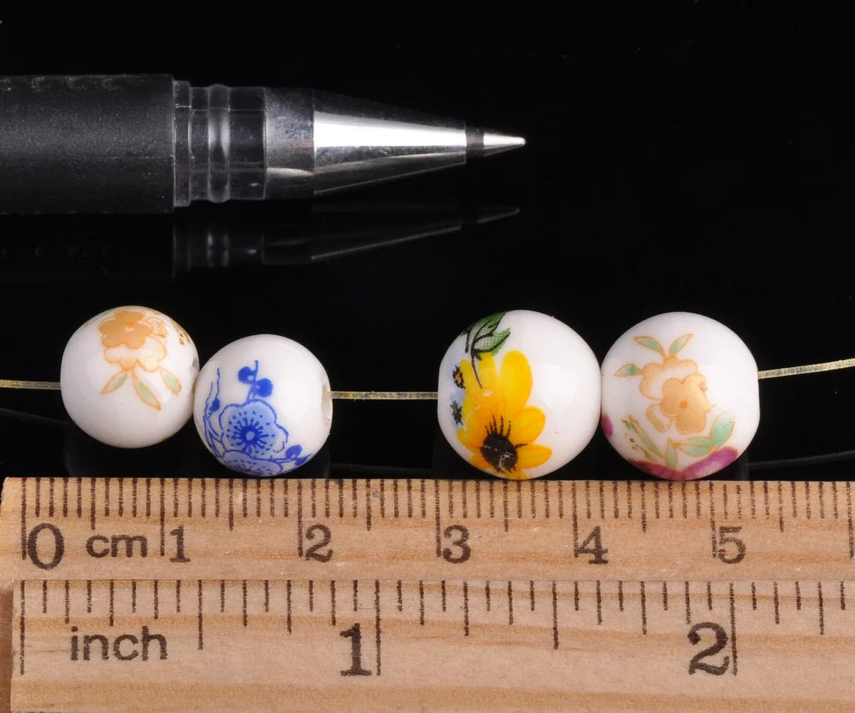 A row of white ceramic beads with floral designs is displayed next to a black pen and a wooden ruler.