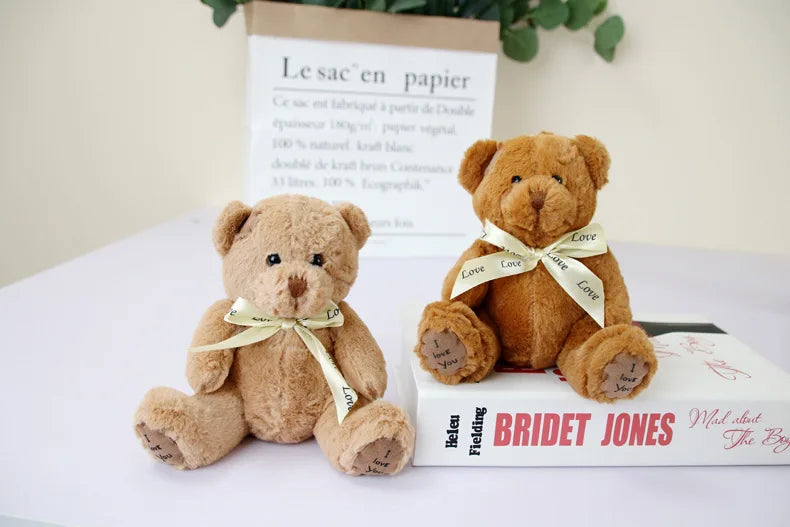A brown teddy bear plush toy with a light yellow ribbon, resting on a book.