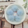 A close-up of light blue fluffy mink fur pom poms displayed in a white bowl on a wooden table.
