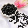 A pile of assorted black pearl beads for jewelry making next to a pink flower.