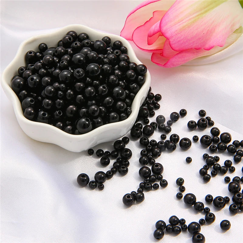 A pile of assorted black pearl beads for jewelry making next to a pink flower.