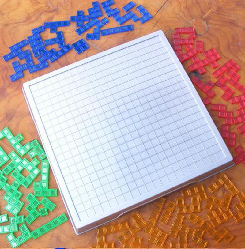 A white grid board is surrounded by various colored plastic blocks including blue, red, and green pieces on a wooden surface.