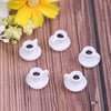 A set of five small white resin coffee cups with black interiors resting on a wooden surface next to a yellow flower.