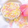 A bowl filled with assorted pink and yellow pearl beads, some spilling out onto a white fabric.