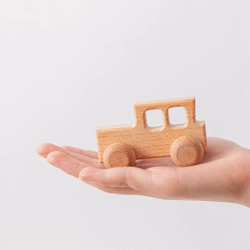 A small wooden car teether toy is held in an open palm.