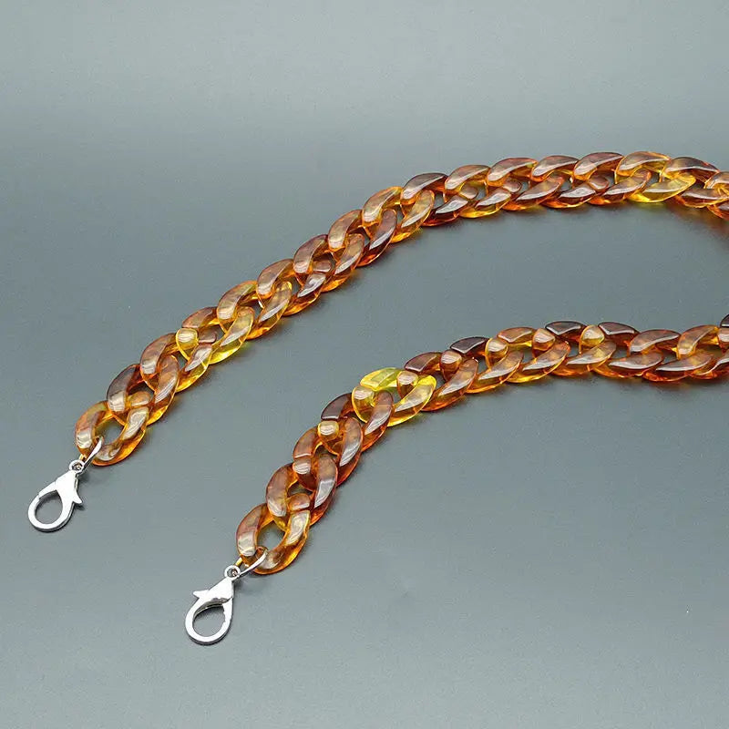 A close-up of an acrylic bag chain strap with clips, featuring a warm amber color.