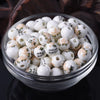 A clear glass bowl filled with small white ceramic beads decorated with delicate floral patterns.
