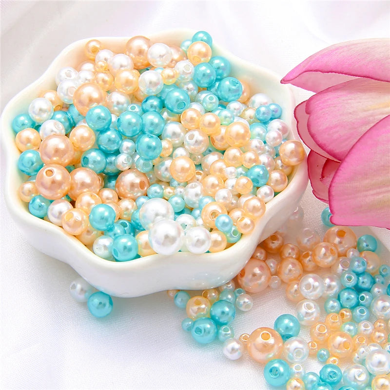 A bowl filled with assorted pearl beads in shades of pink, cream, and blue scattered on a white surface.