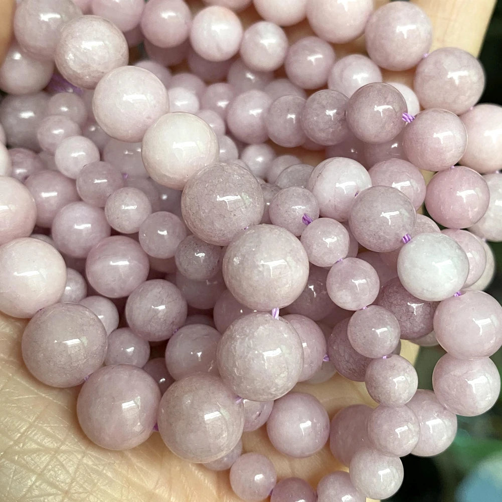 A close-up of small, round natural gemstone beads in various shades of pink and purple.