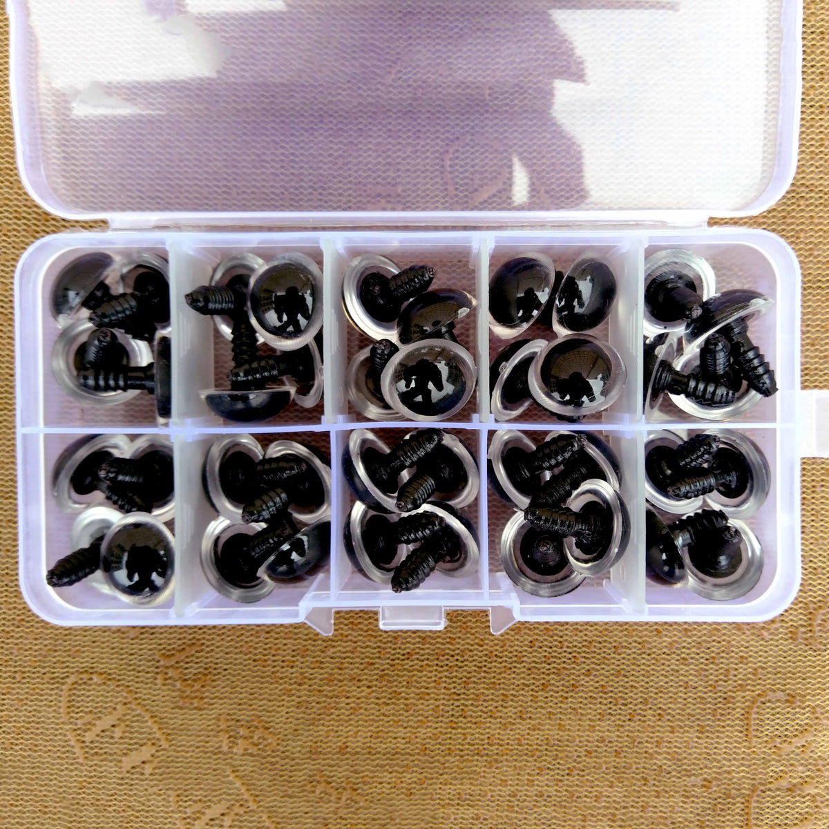 A clear plastic box containing multiple colorful safety eyes for dolls and amigurumi