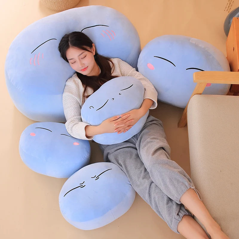 A woman is relaxing while cuddling several blue and light blue plush toys shaped like anime slime characters.