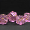 A set of seven translucent pink glitter polyhedral dice resting on a dark surface.
