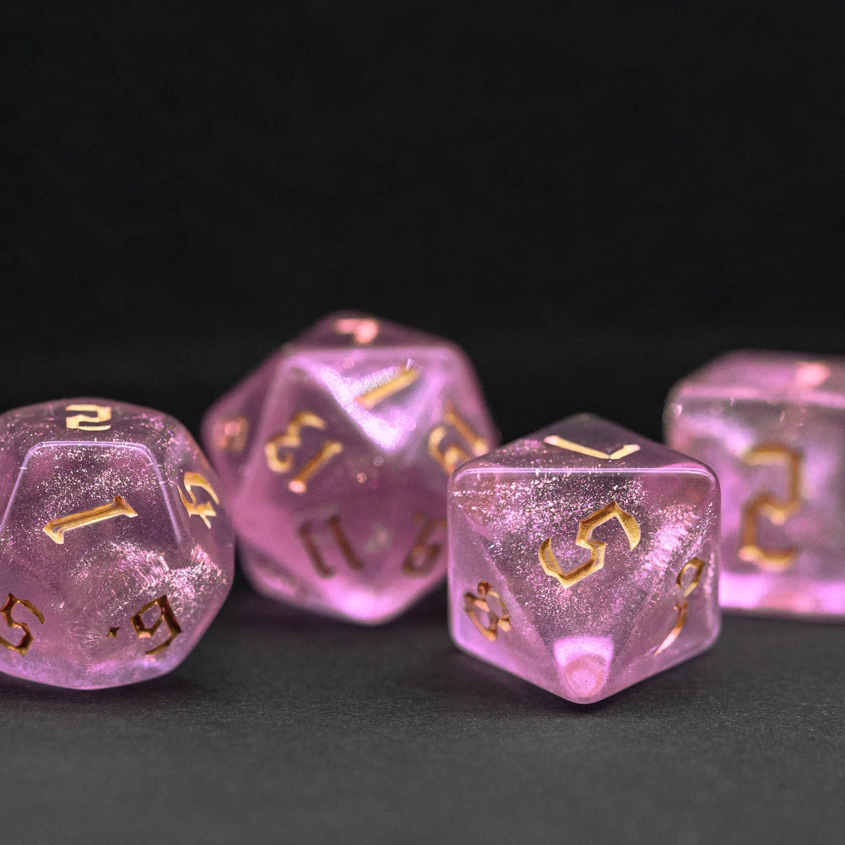 A set of seven translucent pink glitter polyhedral dice resting on a dark surface.